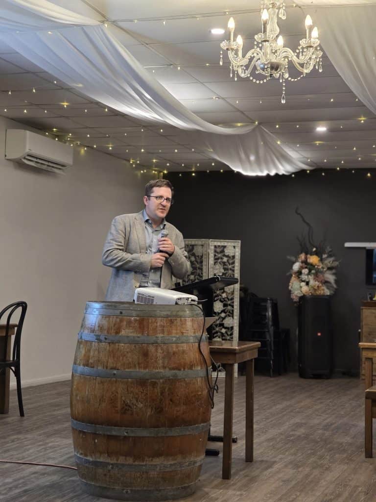 Man speaking at event with decorated ceiling and chandelier, promoting eye health.