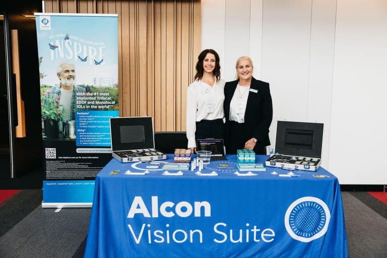 Two women standing behind a booth at the VFLI Conference showcasing Alcon Vision Suite products.
