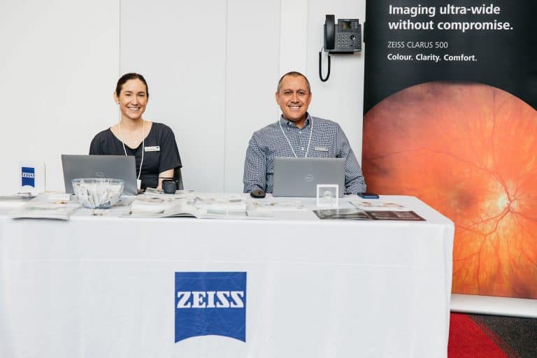 Two smiling professionals at Vision For Life booth showcasing ZEISS imaging technology.